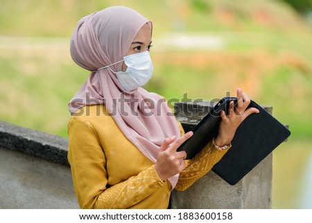 Asian muslim student woman with traditional dress wearing medical face mask at le lake.