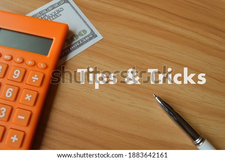 Selective focus with blurred effect of calculator, money banknote and pen over wooden background written with text TIPS and TRICKS. 