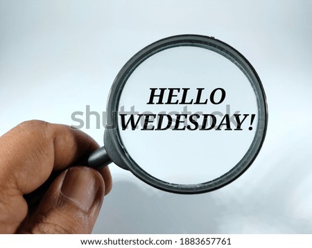 Selective focus.Hand holding magnifying glass with HELLO WEDNESDAY in black word on white background.Education concept idea.