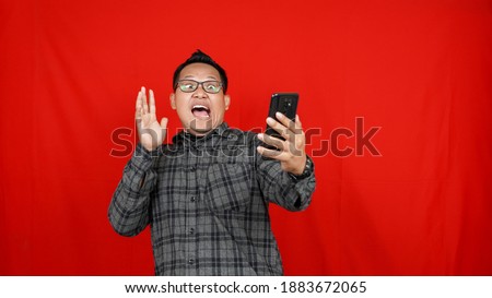 Wow face of Asian man shocked what he see in the smartphone isolated red background