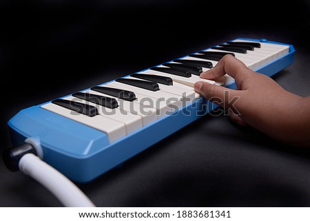 Hand playing pianica blow-organ musical instrument with black background