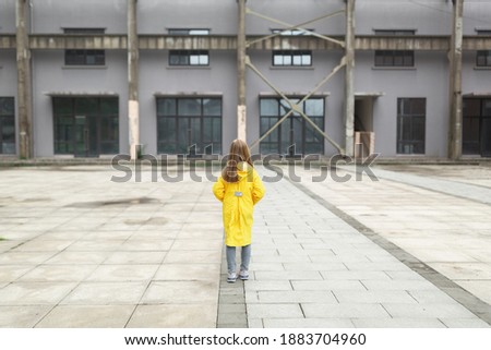little caucasian girl 7 years old with blonde hair in yellow raincoat from behind. Colors of the year 2021 ultimate gray and illuminating