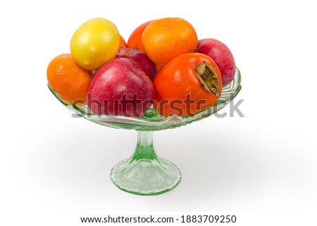Different fresh fruits in a vintage green glass vase for fruits on a leg on a white background
