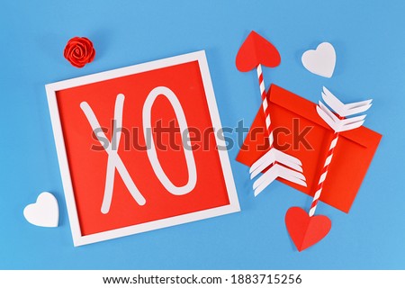 Valentine's Day composition with picture frame with text 'XO', cupid love arrows, letter, and hearts on blue background