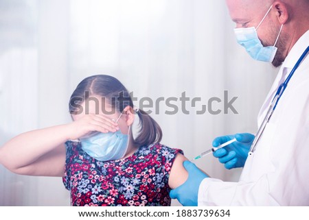 Children vaccinating immunization concept. Doctor injecting vaccination in arm of a scared little girl with face mask.