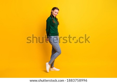 Full length body size photo of shy girl with braids in casual outfit smiling isolated on vivid yellow color background