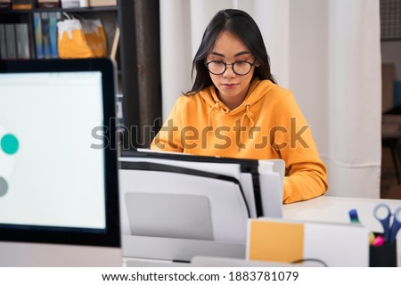 Portrait view of a serious woman designer editing photo on laptop computer in modern office in front of her colleague. Stock photo