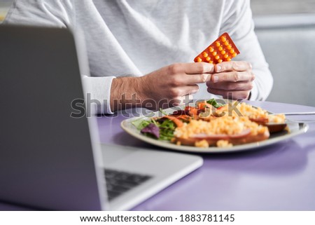 Cropped view of the self care man drinking healthy pills before the meal while preparing to eating at the restaurant or cafe. Stock photo