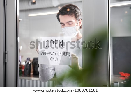 Caucasian waiter wearing protective equipment hanging open sign while reopening restaurant for delivery and takeaway only during coronavirus epidemic