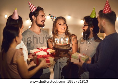 Happy birthday to you. Smiling young woman in her twenties holding her birthday cake with lit candles and thanking her friends for surprise and presents at evening party at home