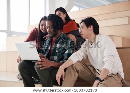 Group of students or teenagers with laptop computer sitting at the stairs and watching something together. Communication, technology , education and teenage concept. Stock photo