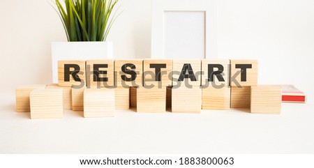 Wooden cubes with letters on a white table. The word is RESTART. White background with photo frame, house plant.