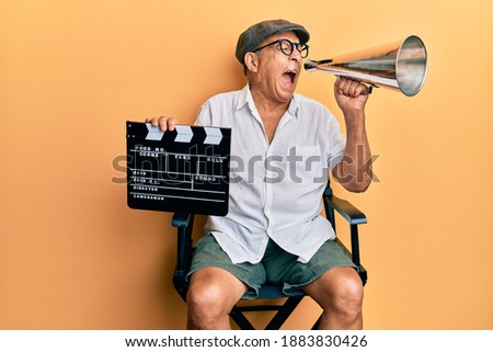 Handsome mature director man holding video film clapboard and louder angry and mad screaming frustrated and furious, shouting with anger. rage and aggressive concept.  Royalty-Free Stock Photo #1883830426