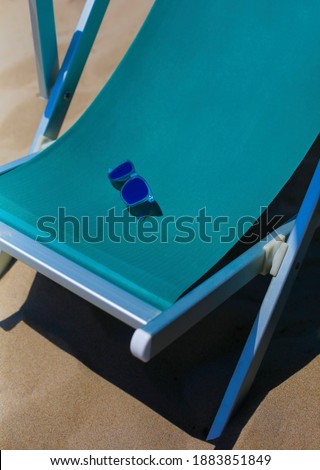 Turquoise sun chaise longue textile chair close up with blue sunglasses on sand, vacation, holiday, resort background  Royalty-Free Stock Photo #1883851849