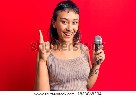 Young woman singing song using microphone smiling with an idea or question pointing finger with happy face, number one 