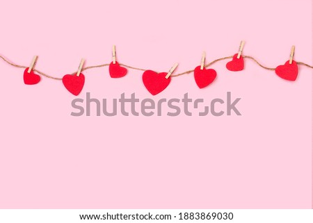 Red paper hearts hanging by a thread on a pink background with copy space