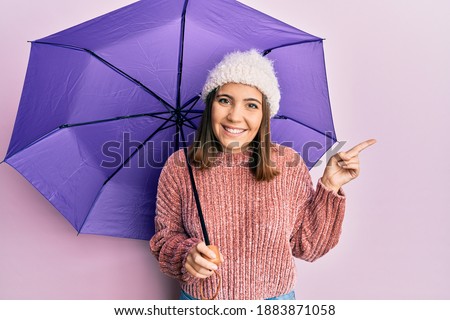 Young beautiful woman holding purple umbrella smiling happy pointing with hand and finger to the side 