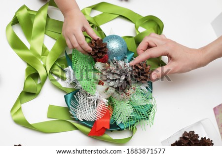 A woman with a child collects a New Year's wreath from satin ribbons and pine cones. The development of creative abilities in a child. Decoration for the new year.