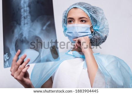 Doctor examines X-ray picture. Woman in protective mask and suit rais her glasses with her hand and hold snapshot of lungs.