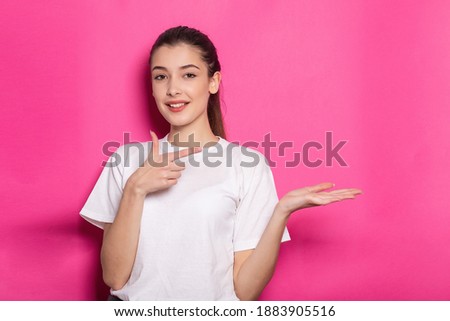 Photo portrait of schoolgirl pointing finger at your product blank space holding hand palm wearing top checkered shirt isolated on pink colored background