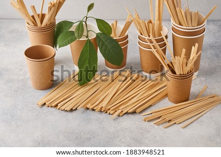 Wooden Drink Stirrers and eco paper glasses with green sprout leaves on grey background. Zero waste and plastic free concept. Top view. Royalty-Free Stock Photo #1883948521