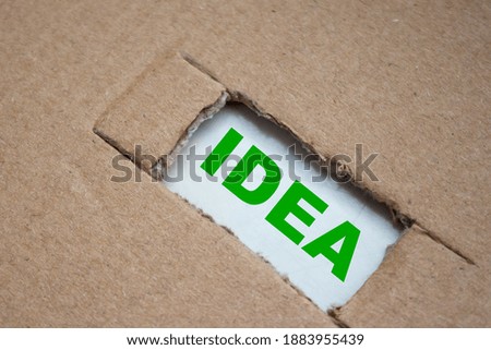 A cut-out hole in the paper cardboard, and under it a piece of paper with the word IDEA. The word IDEA