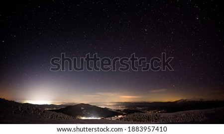 Wonderful night view of the ski resort with hills and slopes against the backdrop of the moon and starry sky. The concept of winter sports and outdoor recreation. Copyspace