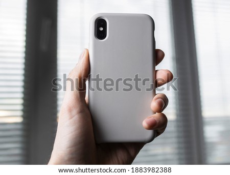Smart phone on the blurred background of the winwow in a white plastic case back view. Smart phone in man's hand. Template of phone case