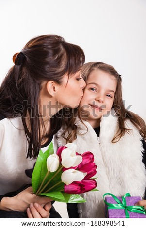 Cute little girl kissing and giving her mother flowers for Mother's day.