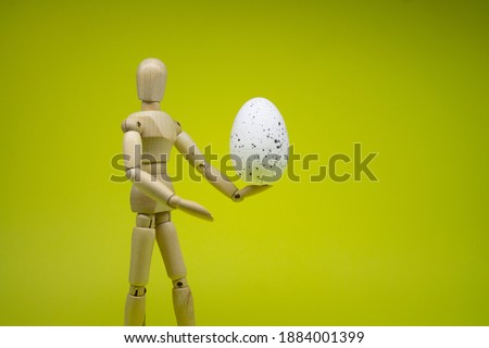 The wooden man holds an egg, congratulates on Easter. Place for text background. Yellow background.