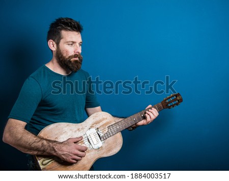 Young caucasian man playing guitar with blue background 