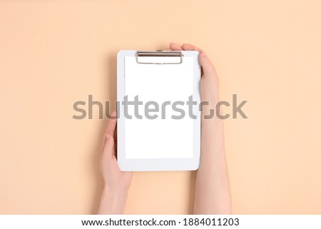 Female hands hold blue clipboard. Clean mockup on a beige background.