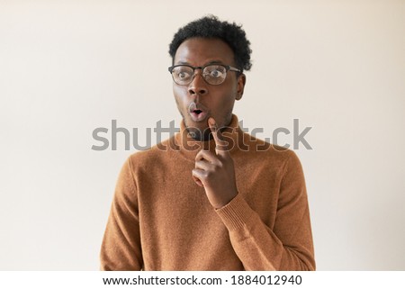 Portrait of handsome Afro American guy in turtleneck sweater raising fore finger and making astonished grimace, having great idea. Emotional young black man expressing astonishment or surprise