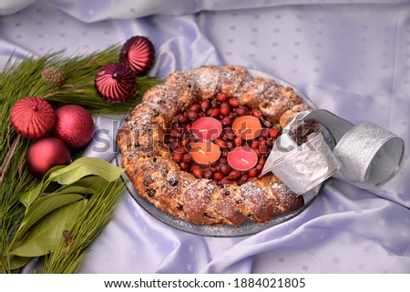 Home baked sweet bread wreath with chocolate yeast dough stuffed with coconut filling on silky tablecloth; Christmas bread with dog rose berries, candles and silver ribbon