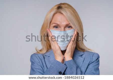 Mature woman in medical mask against Covid 19 is scared isolated over grey background
