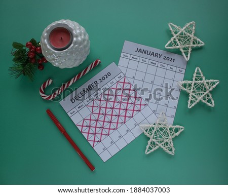 Calendar of December 2020 and January 2021 with red felt-tip pen on green background surrounded by christmas decorations, lollipop and candle. 