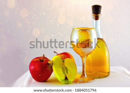 Apples, apple wine in a glass and in a bottle stands on the table on a white sparkling background.
