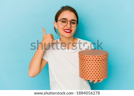 Young skinny arab girl holding a valentines day box showing a mobile phone call gesture with fingers.
