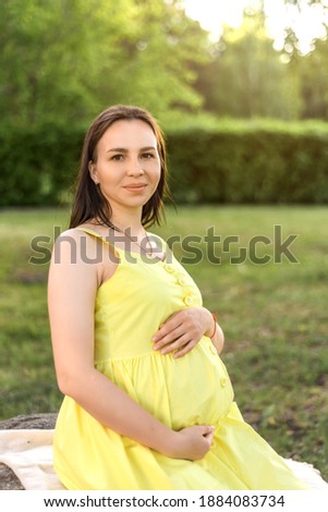 portrait of a pregnant woman on the background of nature and the park. happy pregnant woman in yellow dress in summer