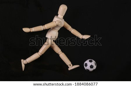 Wooden puppet mannequin playing with soccer ball isolated on black background