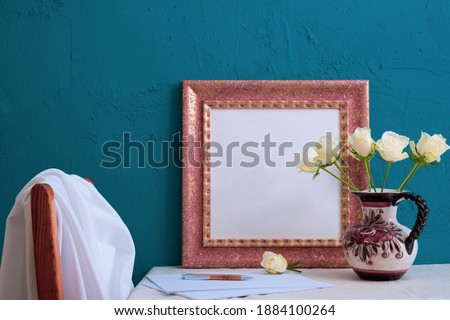 roses in an old vase, set for writing, photo frame on a blue background on the table