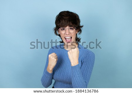Young caucasian woman over isolated blue background very happy and excited making winner gesture with raised arms, smiling and screaming for success.