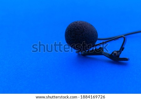Lavalier or lapel microphone on a blue surface, very close-up. The details of the grip clip or bra and the sponge against the wind are visible.