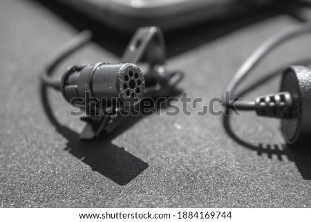 Lavalier or lapel microphone on a black surface, very close-up. The details of the grip clip or bra.