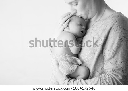 Caucasian mother and son embrace whilst mother kisses newborn son on his head, studio light used.