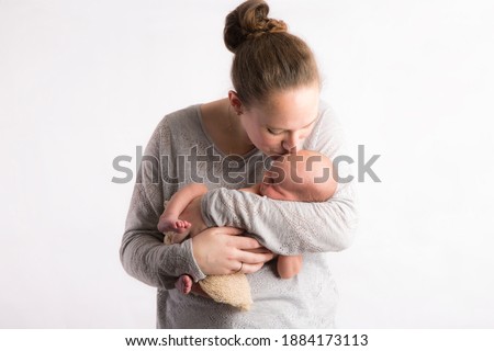 Caucasian mother and newborn son with mother kissing son on his head, studio light used. 