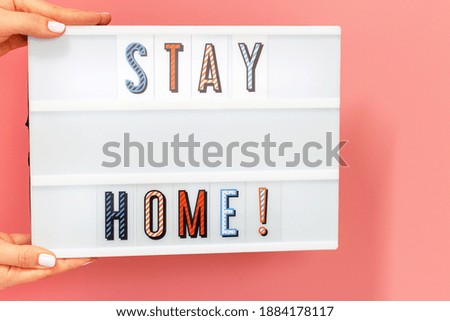 Female hands hold lightbox with stayhome lettering on pink background.