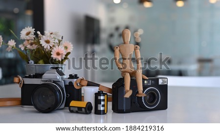 Creative designer or photographer workstation with camera, flower pot and wooden puppet on white table.