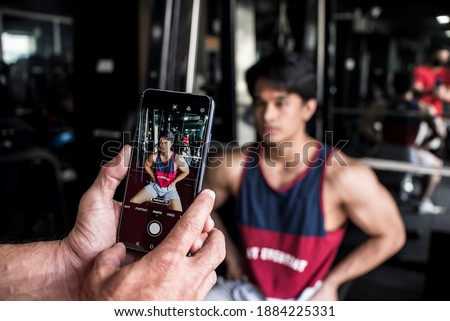 A young fitness model has his picture taken to monitor his progress at the gym. Documenting a person's physical development and muscle gains.