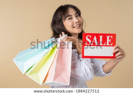 Young woman holding sale message signboard and colorful shopping bags portrait isolated on brown color background